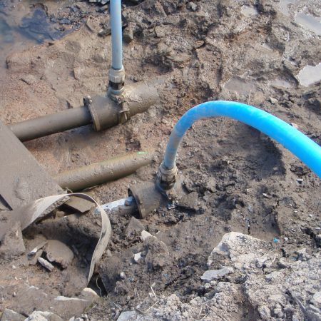 A blue cable going into a pipe covered by mud