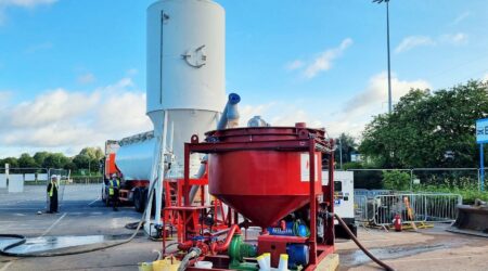 A white silo next to a large red piece of 6m3 machinery